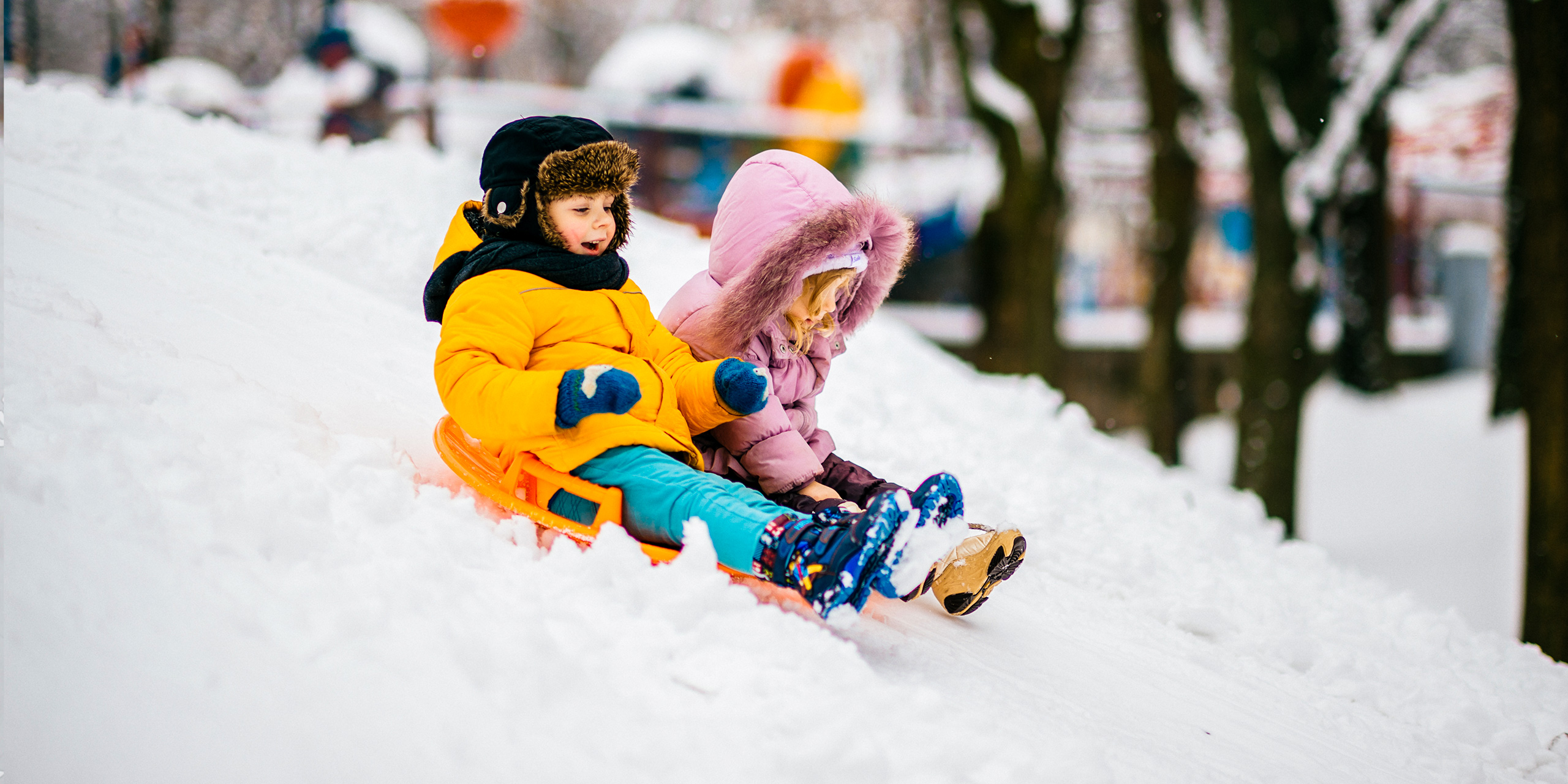 Two small cheerful children ride Board on snow hill;Courtesy of Benevolente82/Shutterstock