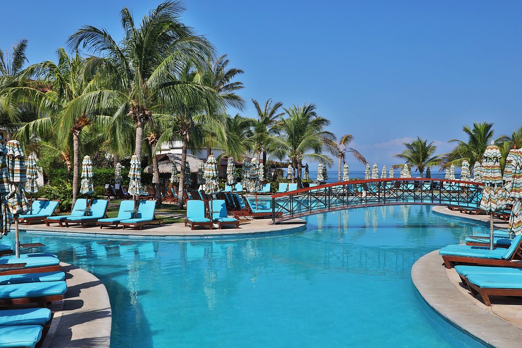 beautiful, large pool with blue chaise lounges around it, bright blue sky and palm trees
