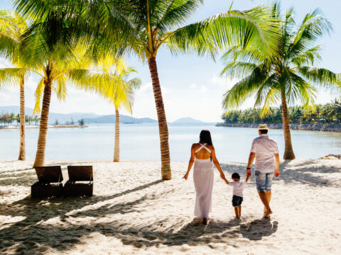 family walking along beach palm trees; Courtesy of shevtsovy/Shutterstock
