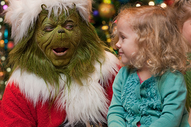 The Grinch sits with a young blond girl at Grinchmas.