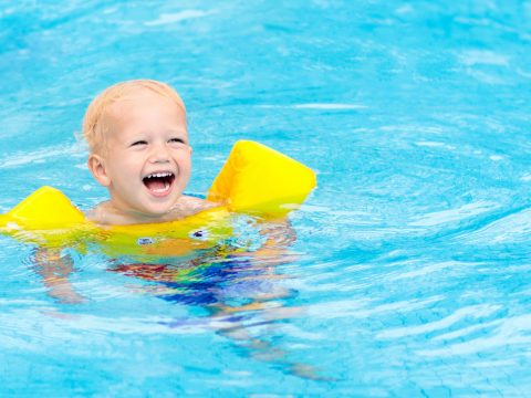 Toddler swimming in pool with swim floaties on; Courtesy of FamVeld/Shutterstock.com