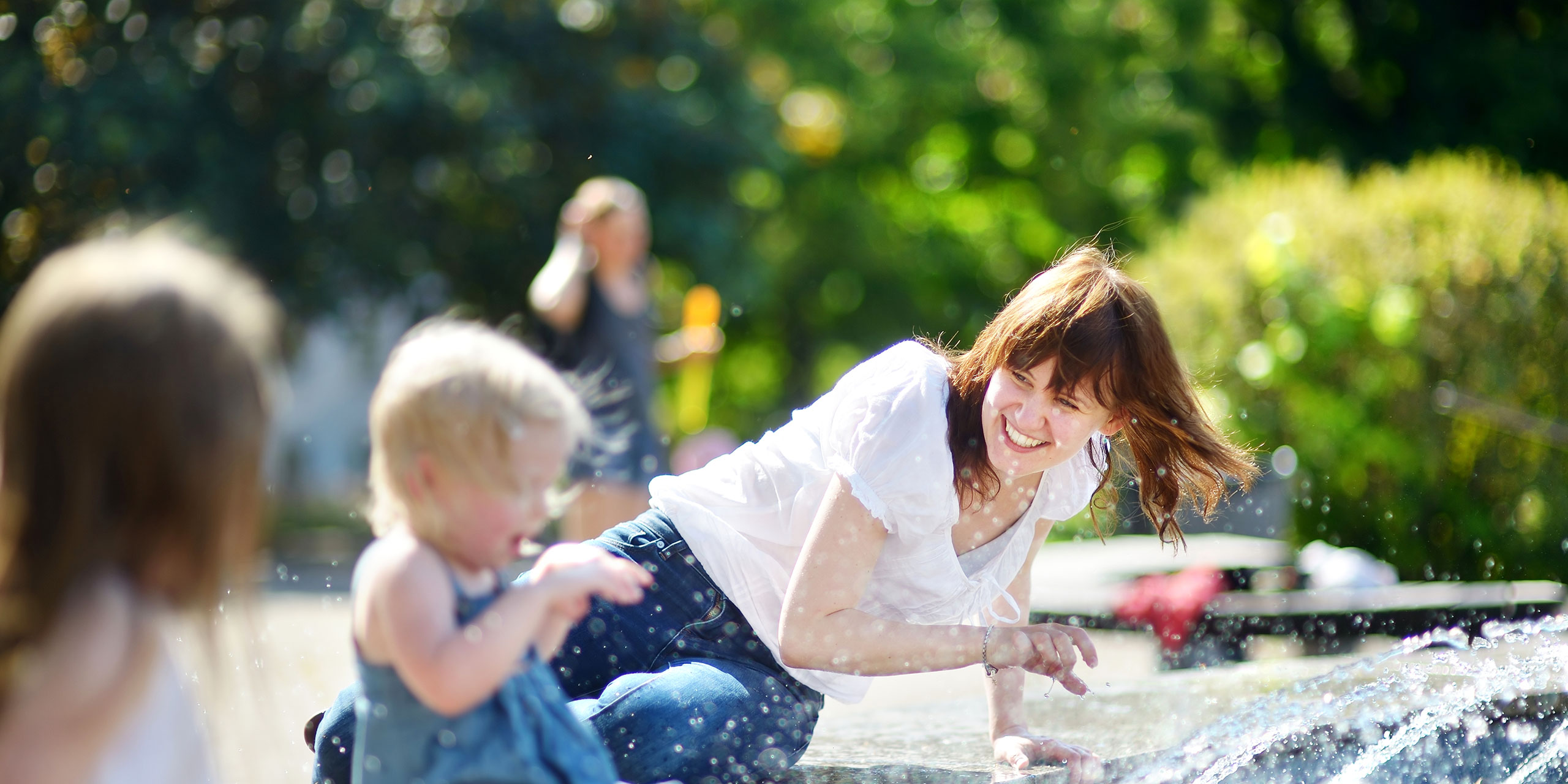 Mom Splashing With Kids at Fountain in City; Courtesy of MNStudio/Shutterstock.com