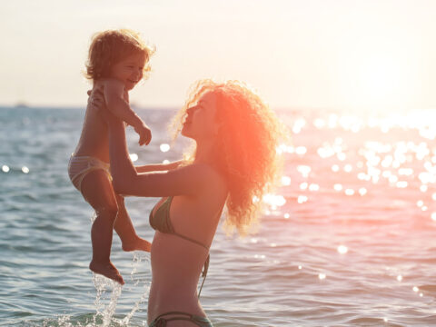 Mom In Two Piece Bathing Suit with Child on Beach; Courtesy of Volodymyr Tverdokhlib/Shutterstock.com