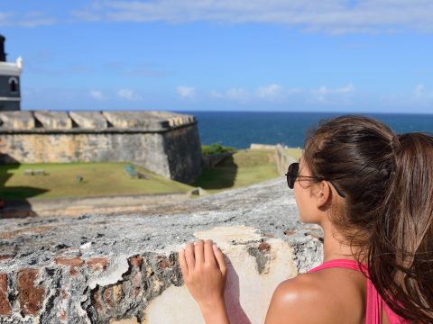 Puerto Rico travel tourist woman in San Juan, looking down at the fort Castillo San Felipe Del Morro; Courtesy of Maridav/Shutterstock