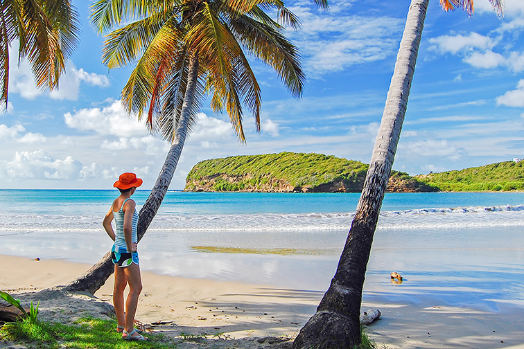 Young woman tourist standing under palm tree on beautiful beach on Grenada island, Caribbean region of Lesser Antilles ;Courtesy of Pawel Kazmierczak/Shutterstock
