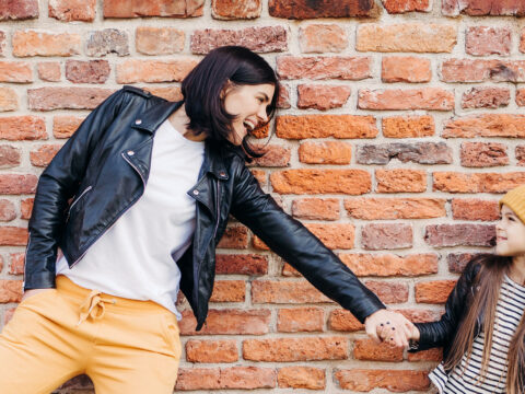 girl and her mother have fun together, keep hands together, pose against brick wall. ; Courtesy of VK Studio/Shutterstock