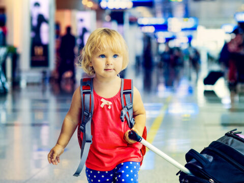 ittle girl with suitcase travel in the airport; Courtesy of NadyaEugene/Shutterstock