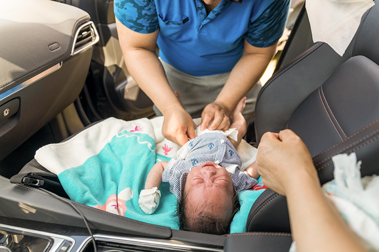 father changing diaper to crying baby in car during picnic. Courtesy of ARTYOORAN/Shutterstock
