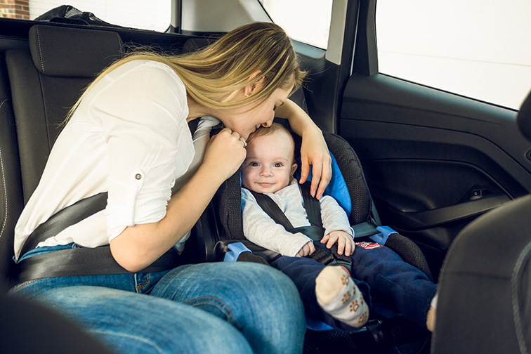 Portrait of happy young mother sitting on back seat with her baby; Courtesy of kryzhov/Shutterstock