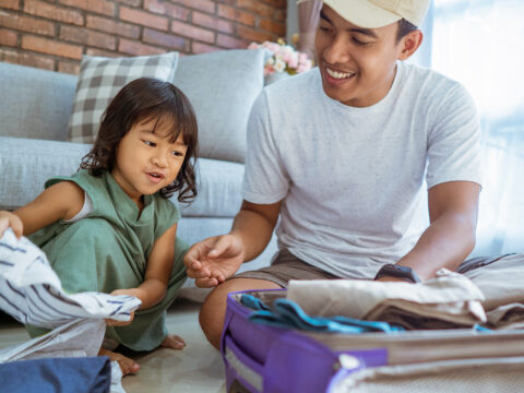 dad and kid happily prepare for holiday. packing up some clothes in suitcase for vacation; Courtesy of Odua Images/Shutterstock