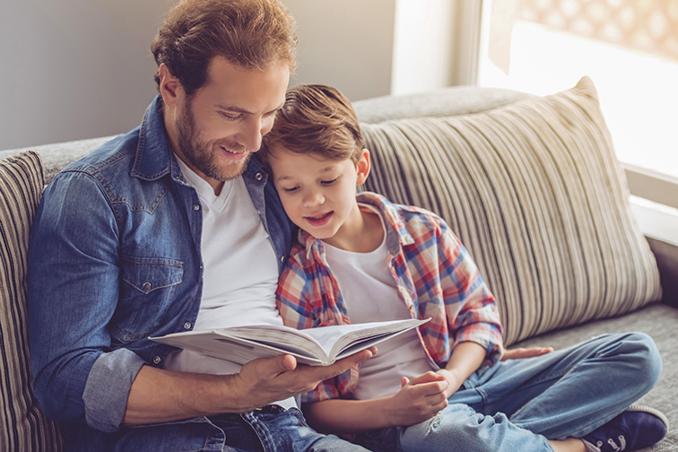 Father and son are reading a book and smiling while spending time together at home; Courtesy of George Rudy/Shutterstock