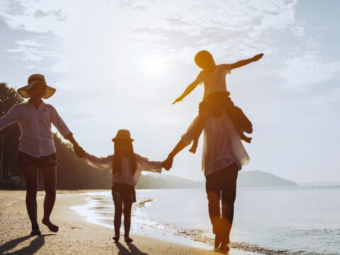 Holiday travel concept, Summer vacations. Happy family are having fun on a tropical beach in sunset. Father and mother and children playing together outdoor on sea.; Courtesy Sumala Chidchoi/Shutterstock