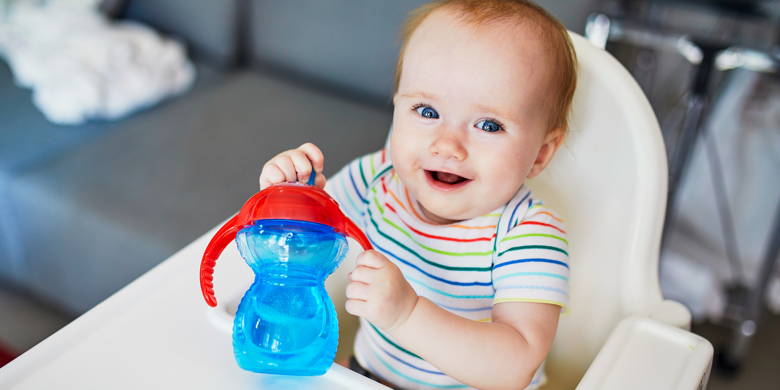 Little baby girl sitting in high chair at home or at restaurant and drinking water from sippy cup; Courtesy Ekaterina Pokrovsky/Shutterstock