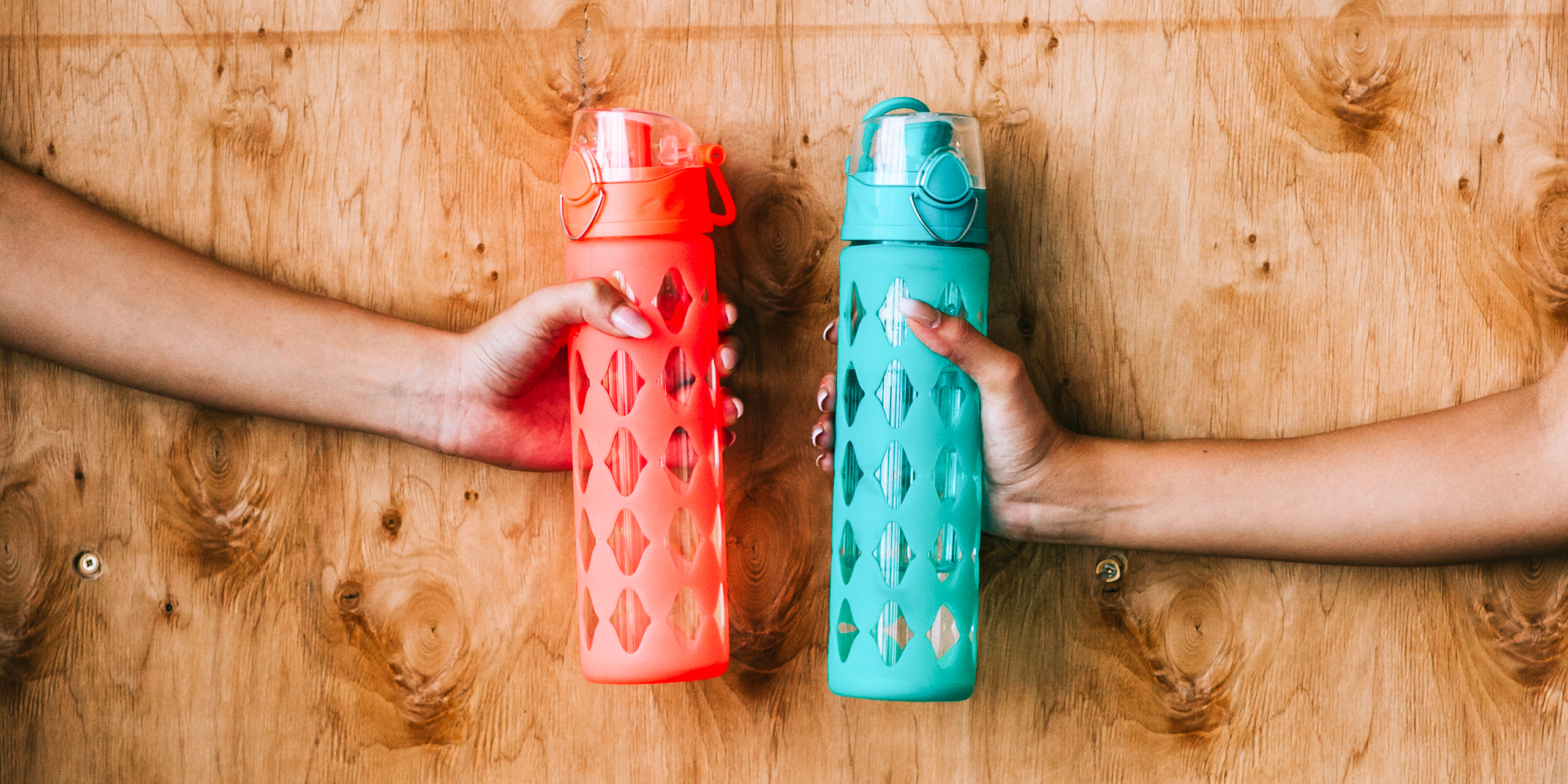 two sports bottle for drinking in women's hands on the wooden background