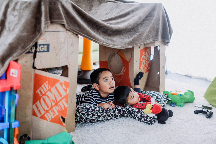 two kids building an indoor fort with pillows and boxes