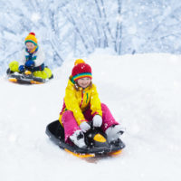 Two children in winter gear sledding down a hill
