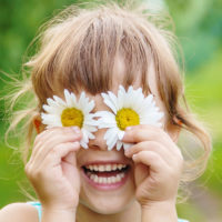Child holding chamomile flowers in front of her eyes