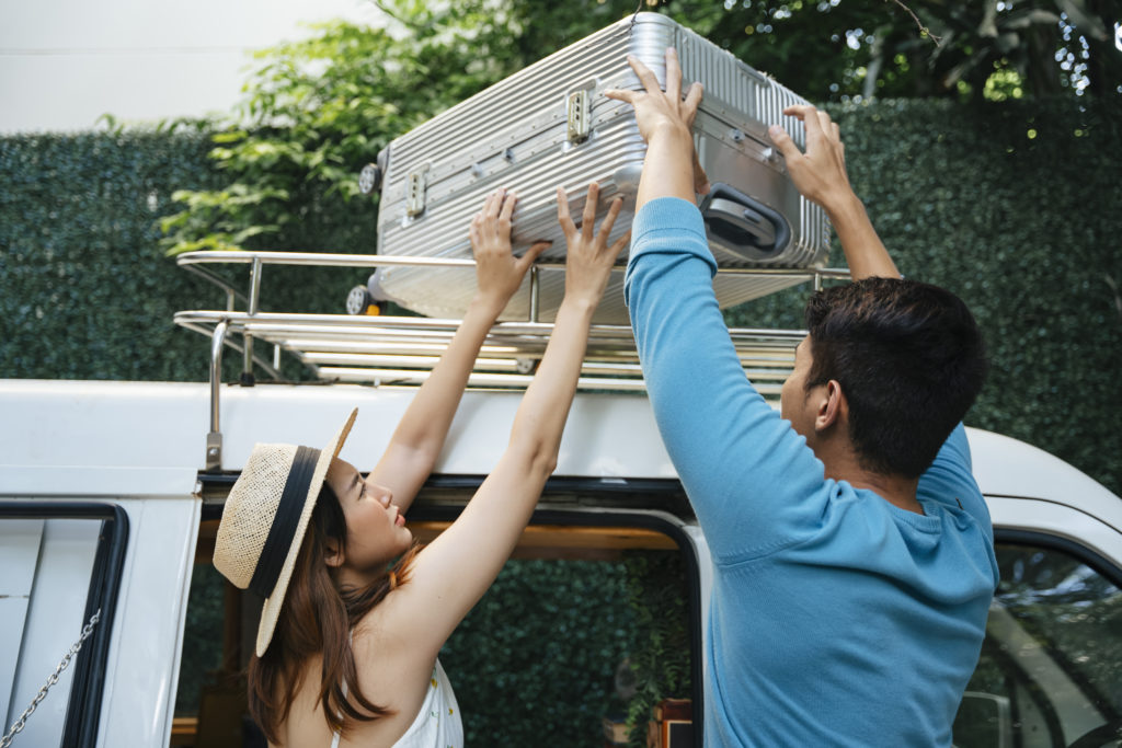 Couple placing a suitcase in the roof rack of a car