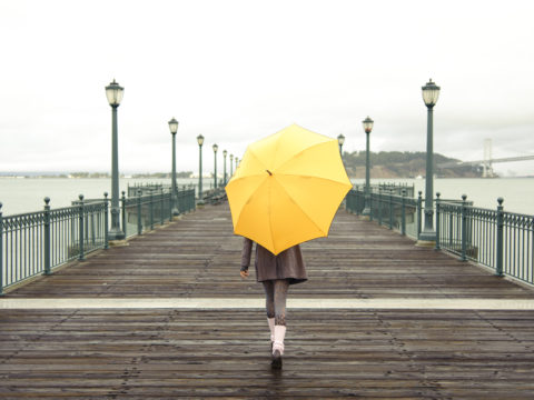 Woman carrying yellow umbrella and walking down a wooden boardwalk