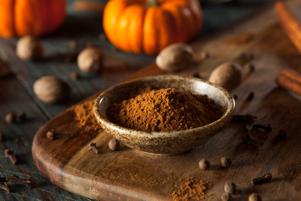 A small, ceramic bowl of pumpkin spice mixture surrounded by small pumpkins and nuts