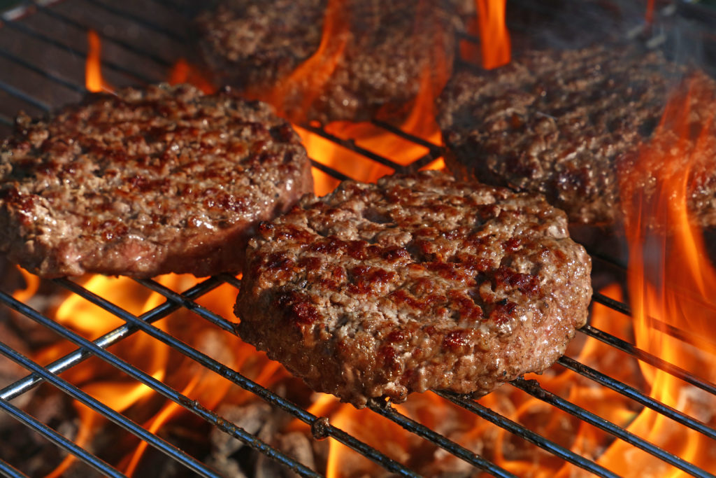 Burgers being grilled over a grill with a high flame