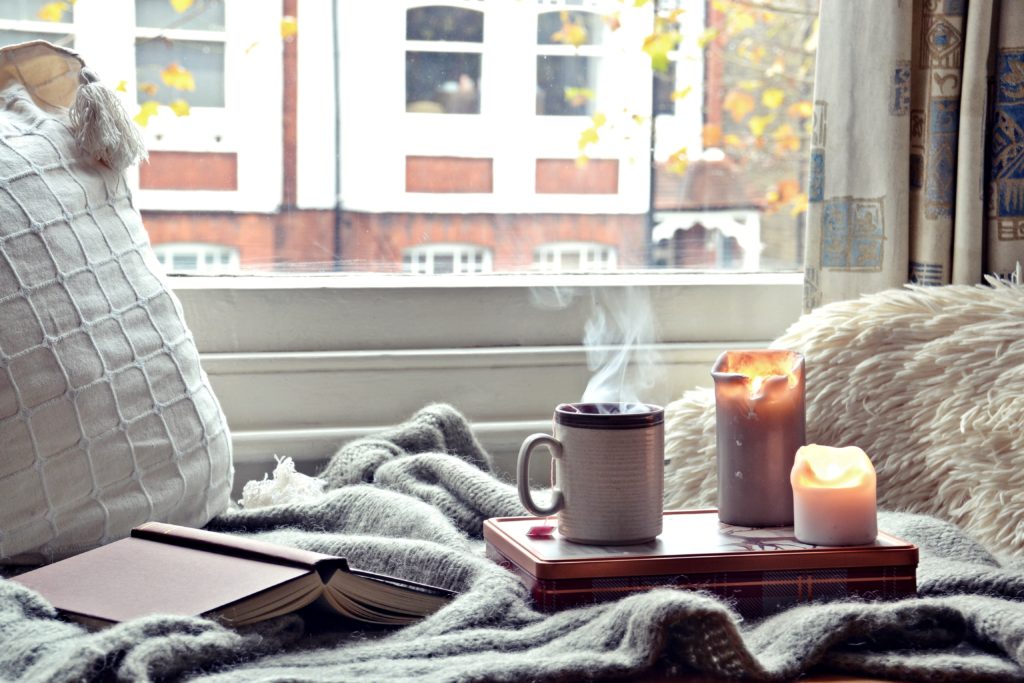 Tray set up with a warm drink in a mug and two candles, set on a blanket near a window