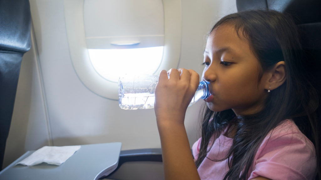 Young child drinking from plastic water bottle on an airplane