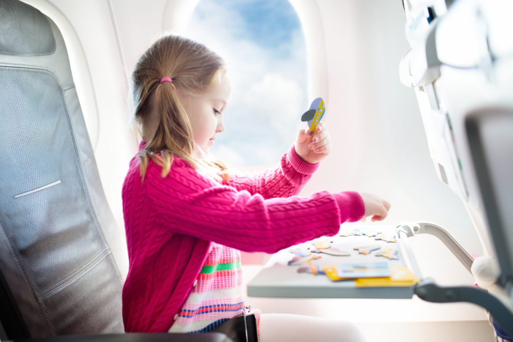 Young child playing a game with cards and cutout airplanes while on an airplane next to an open window