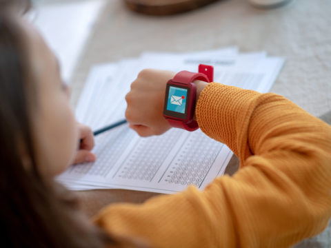 Girl doing homework and looking at her smartwatch, which shows an alert to a new message