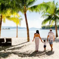 family walking along beach palm trees; Courtesy of shevtsovy/Shutterstock