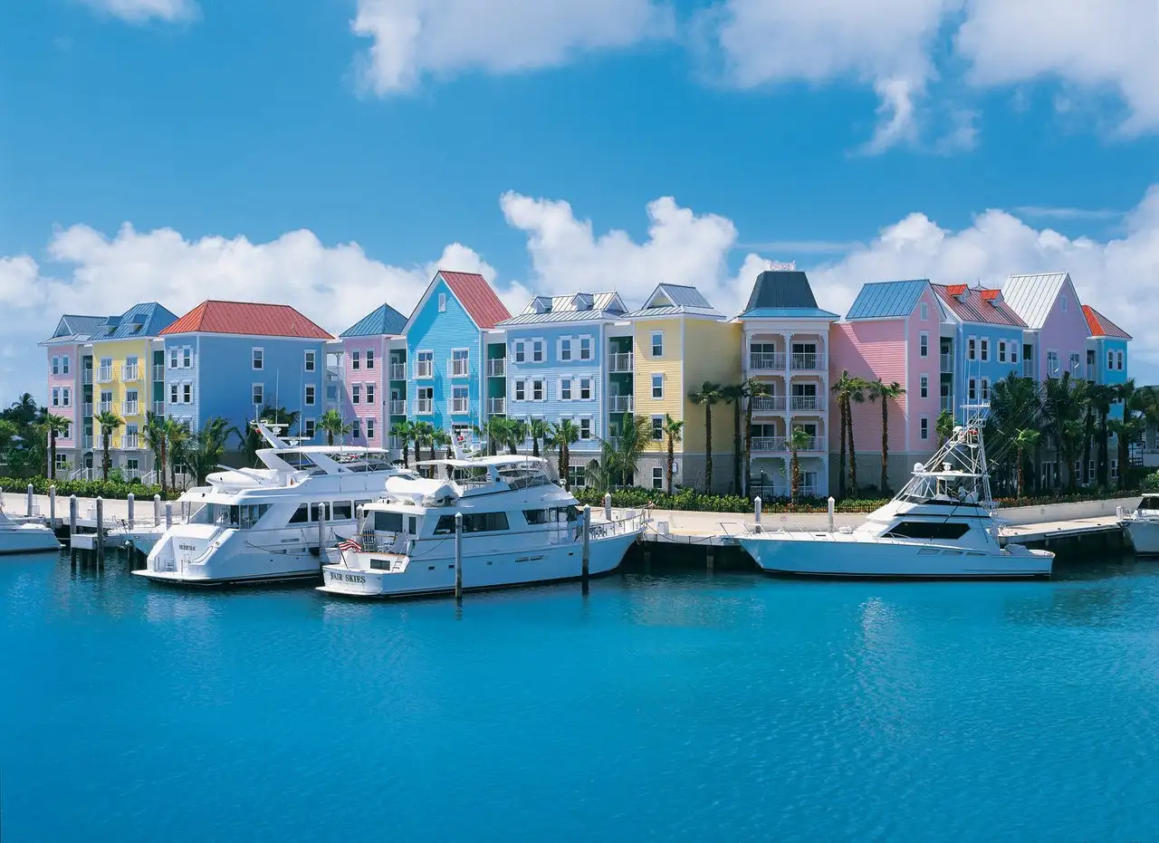 Beautiful blue water with 3 yachts anchored outside of pink, yellow and blue buildings
