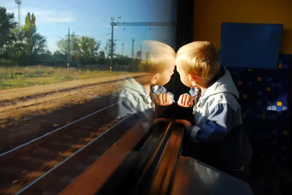 Little boy stares out a train window at passing scenery.