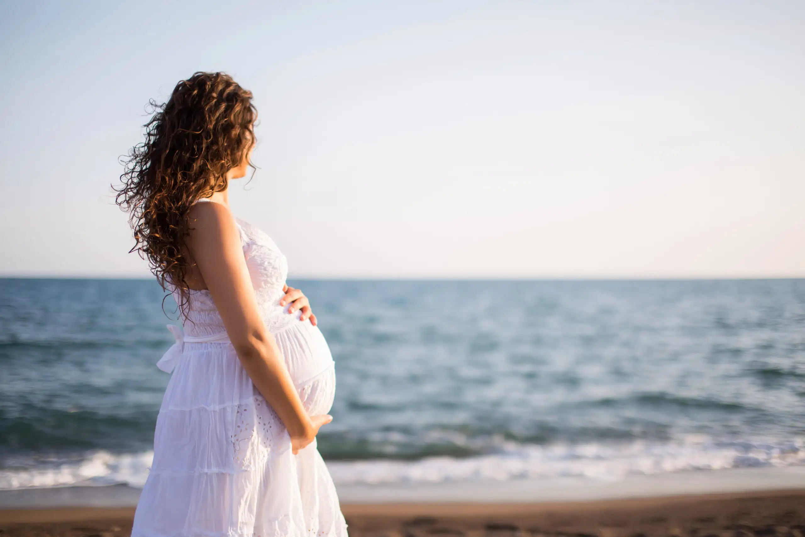 Pregnant woman in white dress standing on the beach