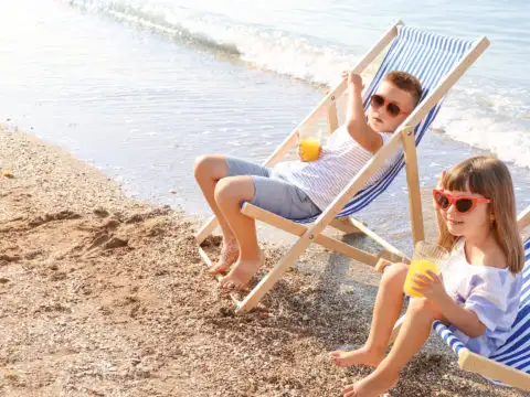 Two children drinking juice on the beach in beach chairs