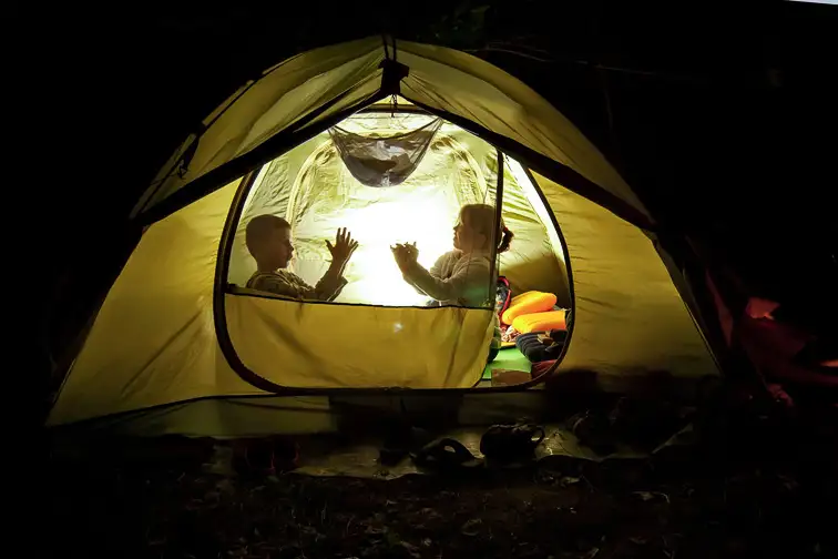 children play in the hike. the tent lights at night from the flashlight. dark silhouettes of children. Courtesy of Ivan Kovbasniuk/Shutterstock