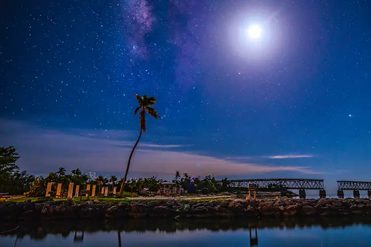 bahia honda state park broken bridge florida keys at night with a moon and milky way stars and palm tree; Courtesy of travelphotoguy/Shutterstock