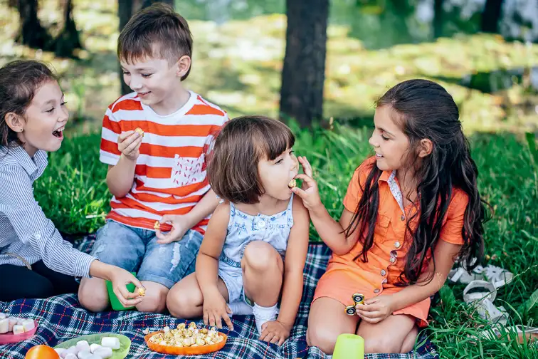 group of kids sitting on a picnic in the woods in the evening rays of sunlight are feed each other; Courtesy of UfaBizPhoto/Shutterstock