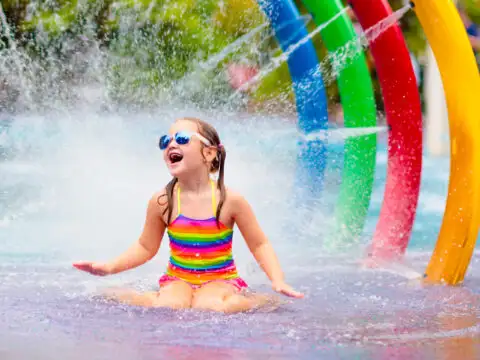 Kids play in aqua park. Children at water playground of tropical amusement park. Little girl at swimming pool. Child playing at water slide on summer vacation in Asia. Courtesy of Famveld/Shutterstock