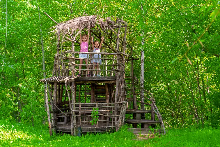 Two little happy girls in a wooden tree house on a sunny day. Sisters rejoice in the summer. The concept of summer.; Courtesy of UfaBizPhoto/Shutterstock