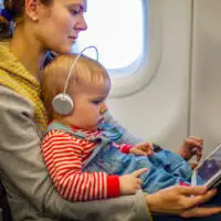 mother and toddler son using tablet pc while on board of airplane; Courtesy of Photobac/Shutterstock