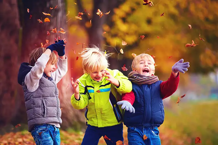 happy friends, schoolchildren having fun in autumn park among fallen leaves; Courtesy of Olesia Bilkei /Shutterstock