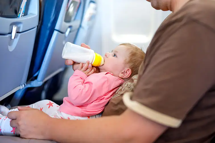 Father holding baby daughter during flight on airplane going on vacation; Courtesy of Romrodphoto/Shutterstock