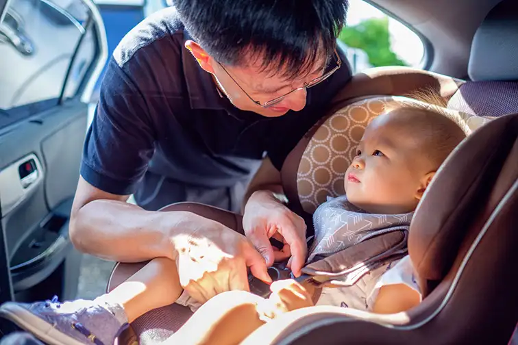 Smiling Middle age asian father helps his cute little asian 1 year old toddler baby boy child to fasten belt on car seat in car before driving; Courtesy of Yaoinlove/Shutterstock