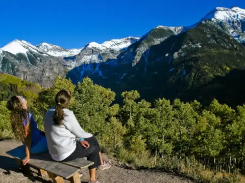 family mom and daughter sit on top of mountain and look at view; Courtesy Colorado Tourism Office