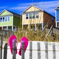 Row of beach rentals on a summer day, pink flip flops on beach fence; Courtesy of StacieStauffSmith Photos/Shutterstock
