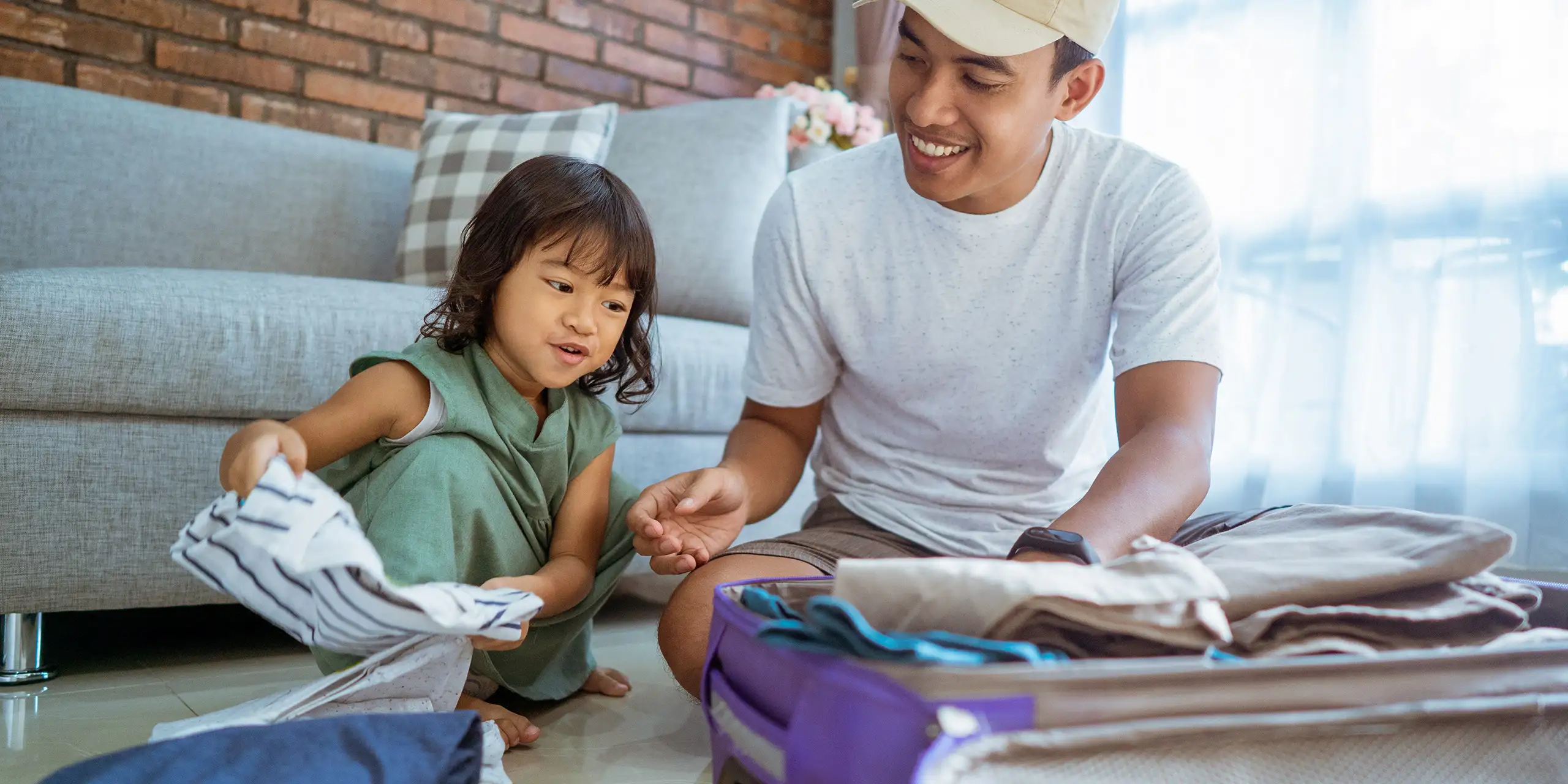 dad and kid happily prepare for holiday. packing up some clothes in suitcase for vacation; Courtesy of Odua Images/Shutterstock