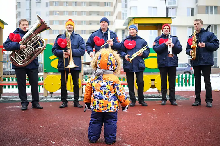 Brass band of six musicians play music and child looks at their on playground at winter day, ; Courtesy of Pavel L Photo and Video/Shutterstock
