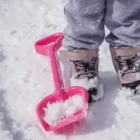 Child wearing snow boots in the snow next to a snow toy shovel