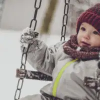 Toddler bundled in snow gear on a swing