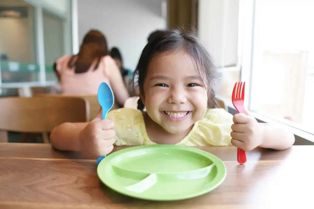 Child holding fork and knife at table